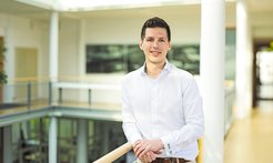 Dr. Adrian Bunzel steht im weißem Hemd am Geländer des Foyes im MPI in Marburg.